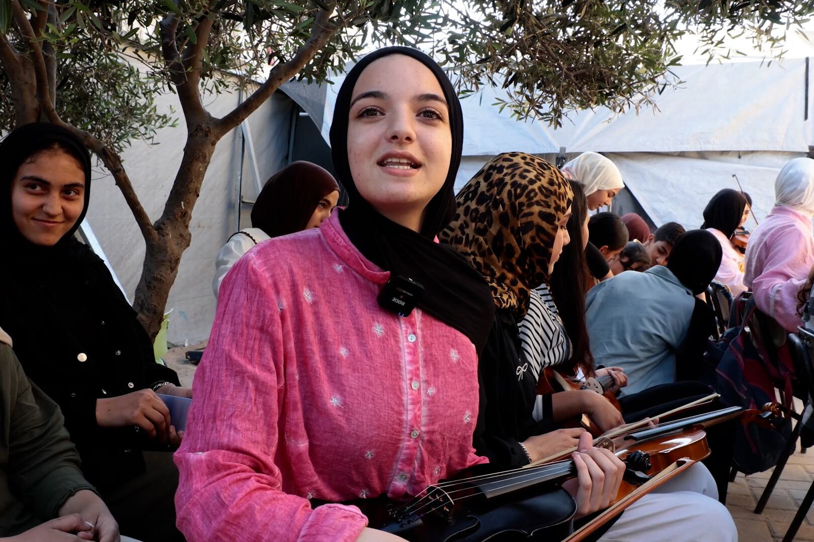 حنان غزال تحمل كمانًا أثناء جلوسها مع طلاب آخرين في معهد إدوارد سعيد الوطني للموسيقى في غزة.