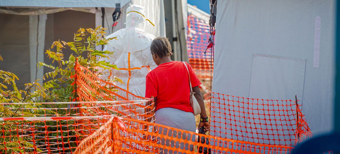 Un trabajador sanitario con un traje protector integral se encuentra junto a una mujer con una camiseta roja en un hospital de campaña en Bunia, República Democrática del Congo.