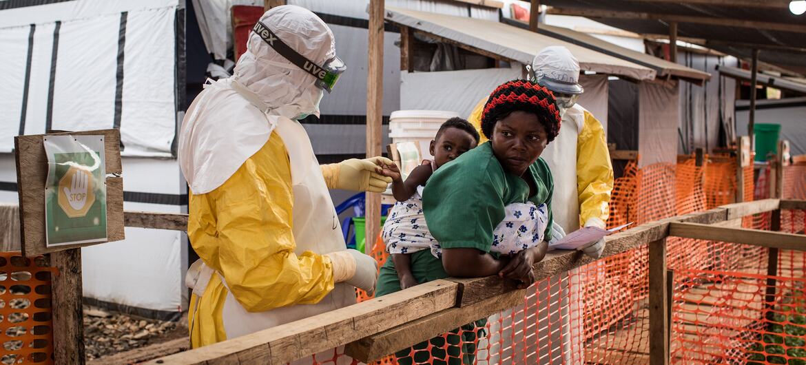 A health worker in a full-body protective suit examines a child being held by a caregiver at a treatment centre in Beni, DRC.