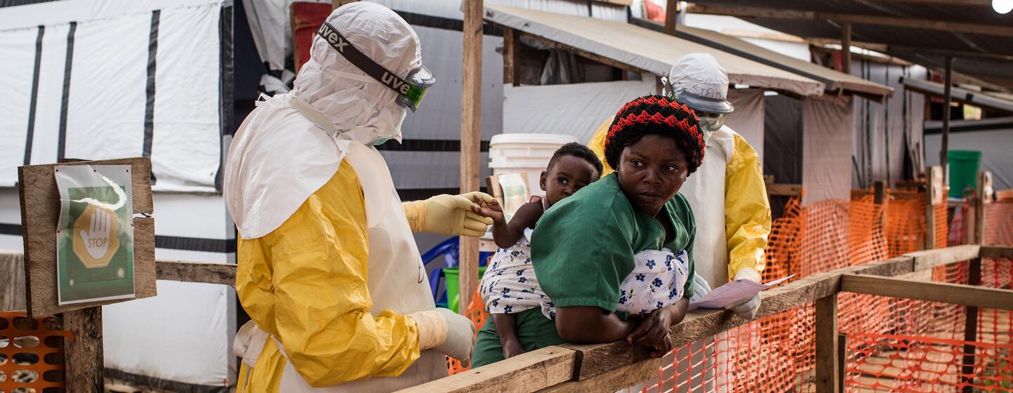 Un agent de santé vêtu d'une combinaison de protection intégrale examine un enfant tenu par un soignant dans un centre de traitement à Beni, en RDC.