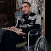 سعيد بكرون، رجل كفيف في غزة، يقرأ من كتاب بطريقة برايل وهو جالس على كرسي متحرك.