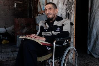 سعيد بكرون، رجل كفيف في غزة، يقرأ من كتاب بطريقة برايل وهو جالس على كرسي متحرك.
