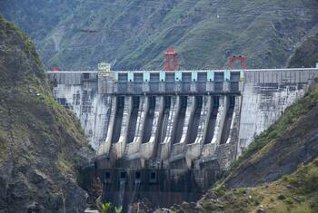 Una gran presa de hormigón atraviesa un valle de montaña, y el agua se libera a través de múltiples aliviaderos.