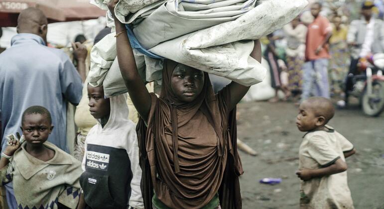 Una niña africana en un campo de refugiados lleva un gran fardo con sus pertenencias sobre la cabeza, rodeada de otros niños en Goma.