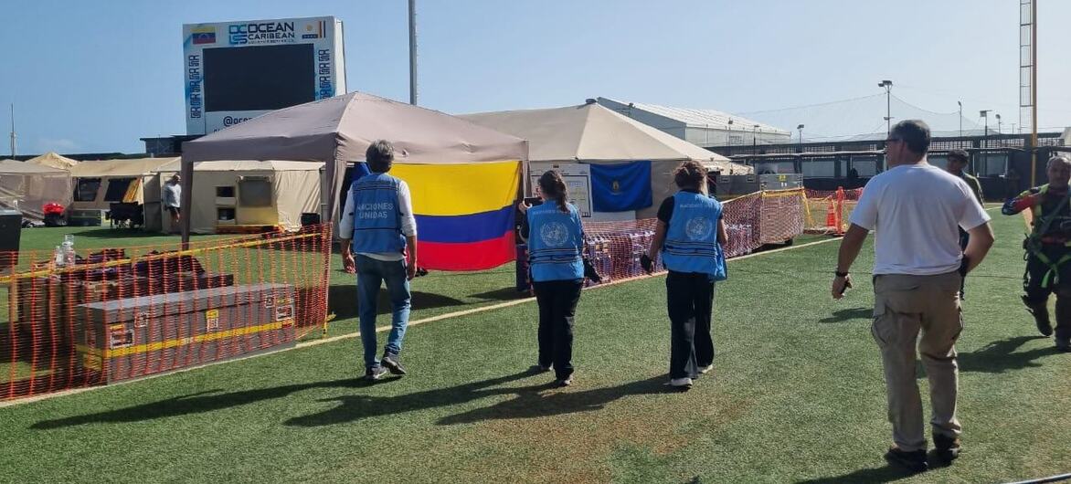 Los trabajadores humanitarios caminan hacia las tiendas de campaña provisionales en un campamento de ayuda, donde ondea prominentemente una bandera venezolana.
