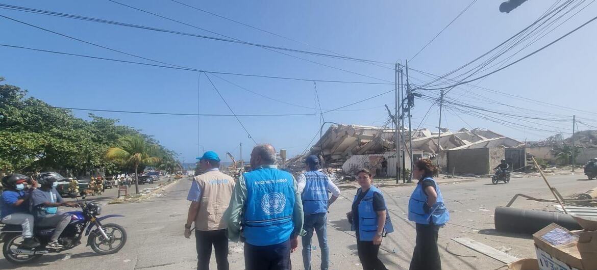 Humanitarian aid workers in blue vests stand on a street near a collapsed building in Venezuela after an earthquake.
