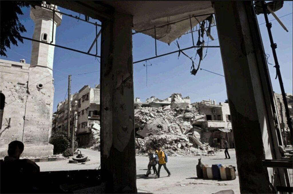 Bâtiments endommagés et décombres dans une rue ravagée par la guerre en Syrie, avec le minaret d'une mosquée visible en arrière-plan.