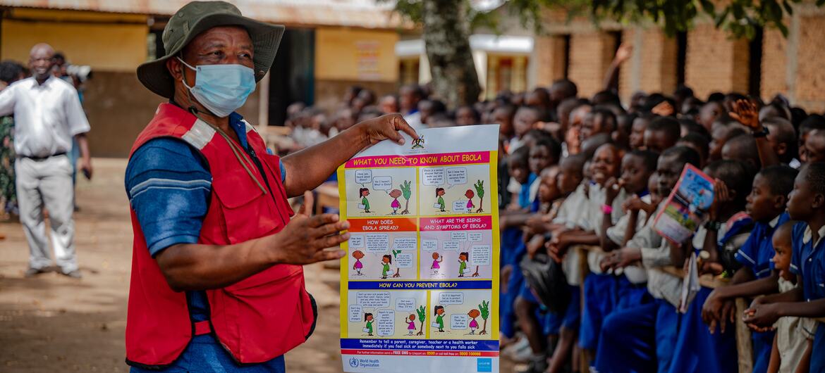 Red Cross volunteer in Uganda teaches Ebola prevention to primary school students using an educational poster.