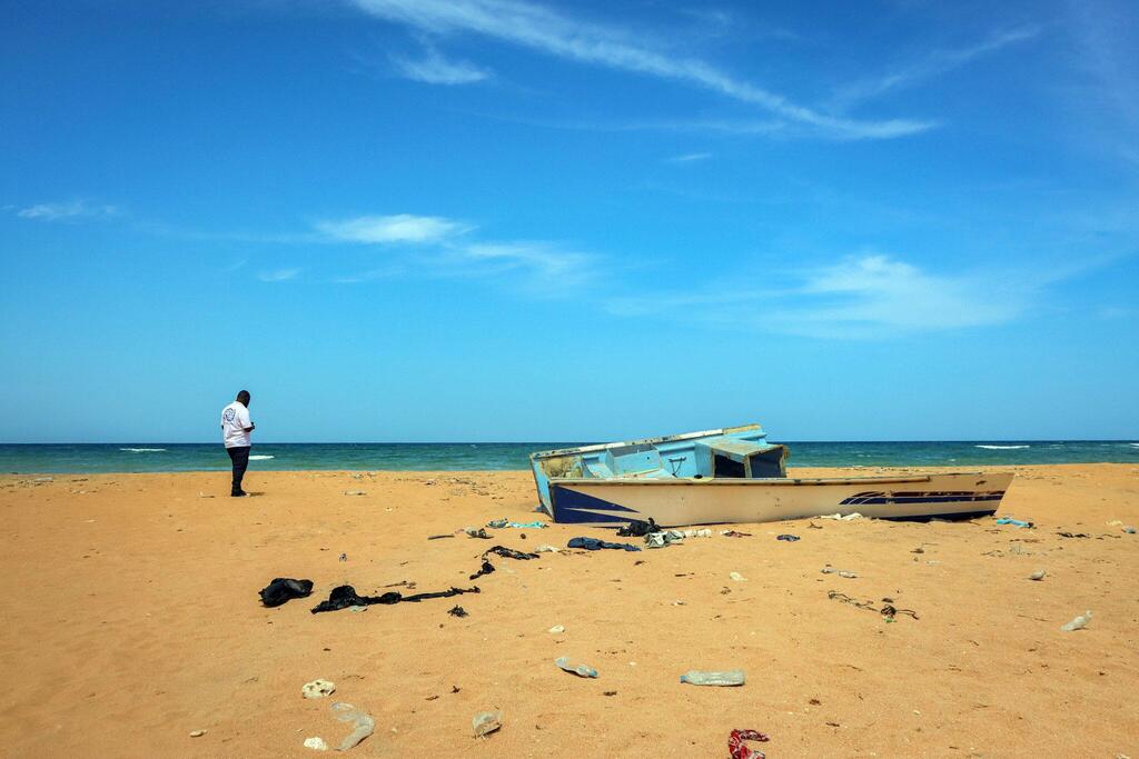 Mashua iliyokwama kwenye ufuo wa mchanga huko Djibouti, na mwanamume amesimama karibu chini ya anga safi la bluu.