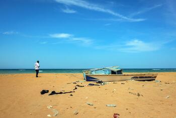 Un bateau échoué sur une plage de sable à Djibouti, avec un homme debout à proximité sous un ciel bleu azur.