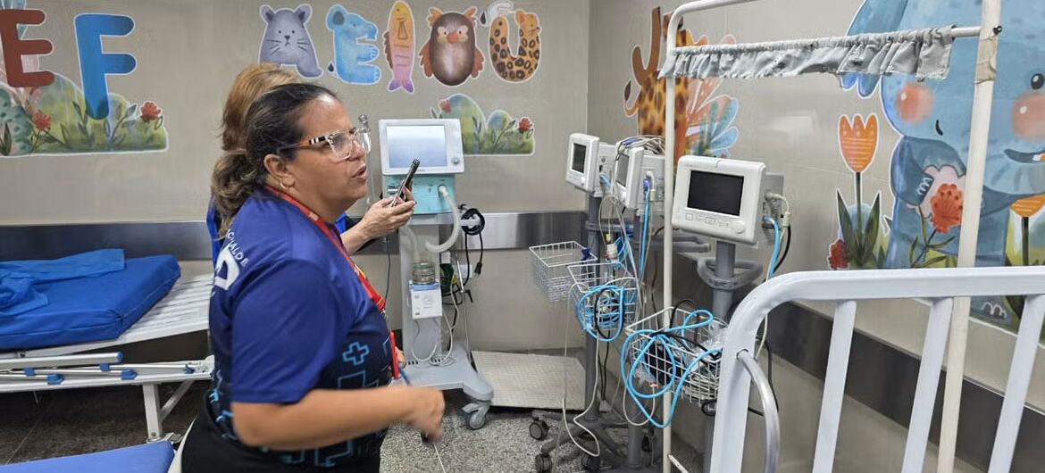 Una enfermera con uniforme azul revisa el equipo médico en una habitación de hospital infantil decorada con coloridos dibujos de animales y mariposas en las paredes.