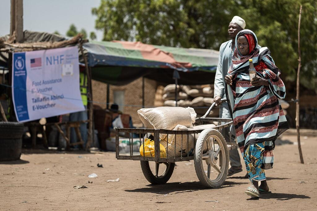 Mwanamume na mwanamke mzee wa Nigeria wakisukuma mkokoteni uliojaa mgao wa chakula cha msaada katika kituo cha usambazaji WFP huko Dikwa, Jimbo la Borno, Nigeria.