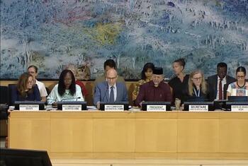 مسؤولون في اجتماع UN Human Rights Council في جنيف، مع لوحات تحمل أسماء الرئيس والأمين العام والمفوض السامي لحقوق الإنسان على الطاولة.