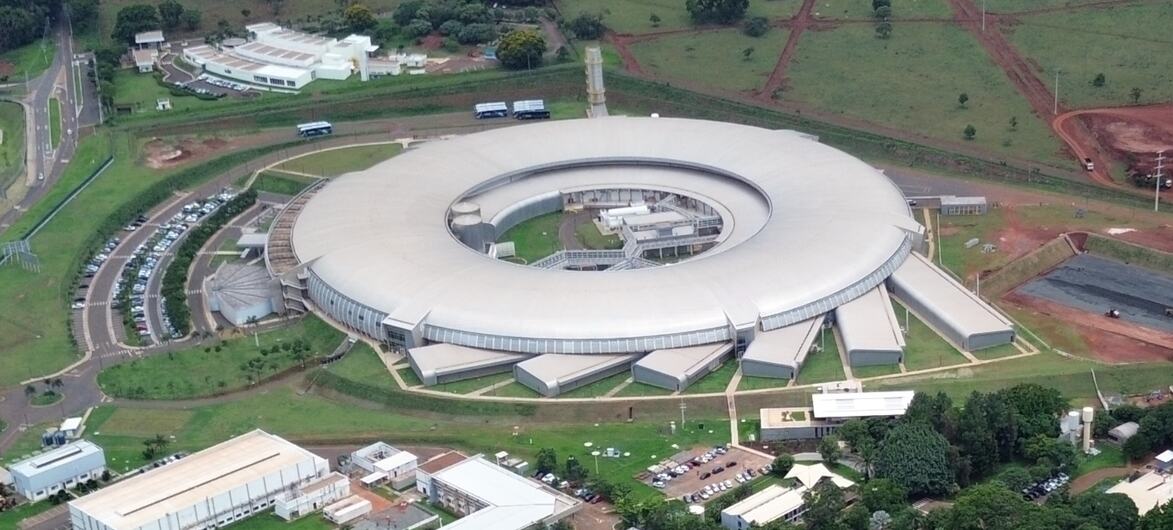 Vista aérea de um grande e moderno complexo de edifícios circulares, rodeado por campos verdes e edifícios menores do campus.