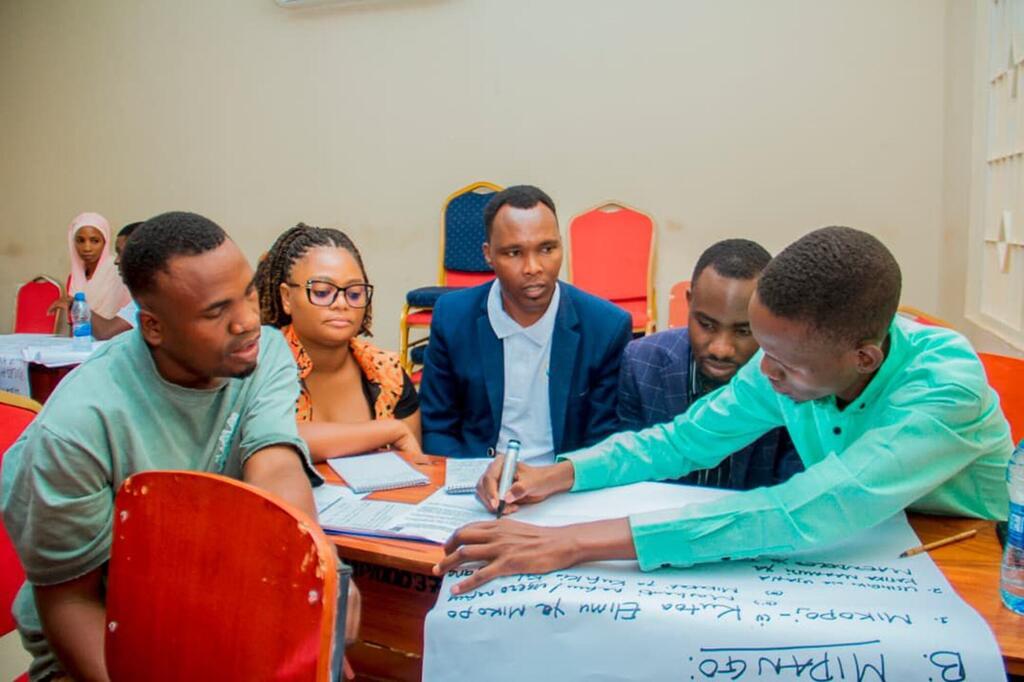 Vijana wanashiriki katika warsha ya UNDP nchini Tanzania, wakifanya kazi kwa ushirikiano kwenye karatasi kubwa mezani.