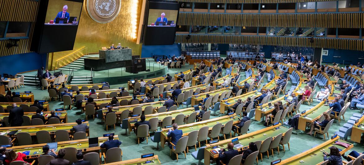 Vista panorámica de la reunión de la Asamblea General de las ONU en Nueva York, con los delegados sentados en un gran salón y el emblema de la ONU visible en la pared.