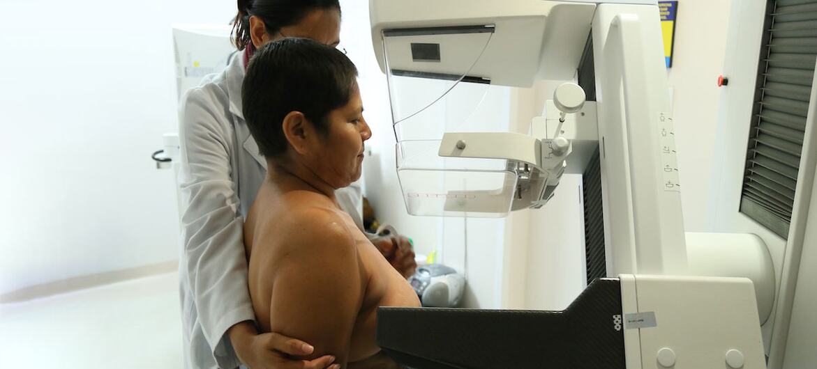 Uma profissional médica auxilia uma mulher mexicana na realização de uma mamografia utilizando um aparelho LORAD em um ambiente clínico.