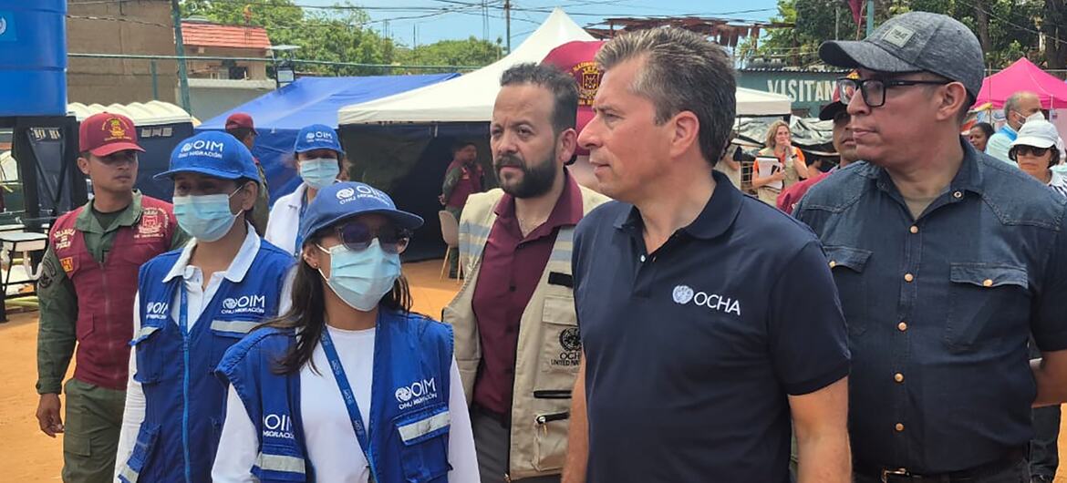 Un grupo de hombres y mujeres, entre ellos personal de la ONU y de la OIM, caminan por un campamento de ayuda humanitaria en Venezuela.