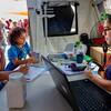 Un trabajador sanitario utiliza un ordenador portátil y un estetoscopio en un puesto médico para ayudar a una mujer y a un niño tras un terremoto.