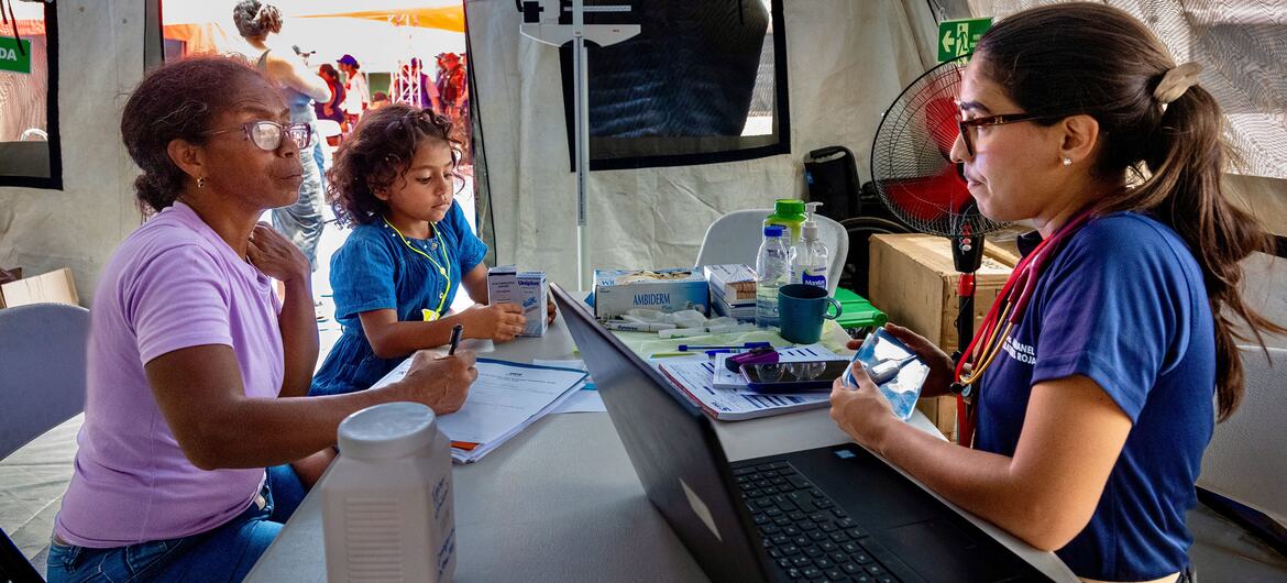 Un trabajador sanitario utiliza un ordenador portátil y un estetoscopio en un puesto médico para ayudar a una mujer y a un niño tras un terremoto.