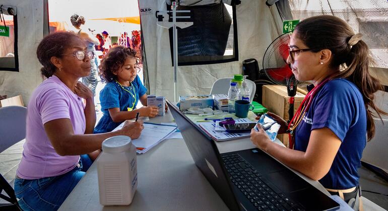 Un trabajador sanitario utiliza un ordenador portátil y un estetoscopio en un puesto médico para ayudar a una mujer y a un niño tras un terremoto.