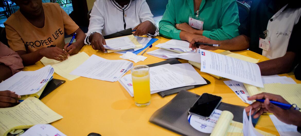 Students participate in a workshop at the Anti-Corruption Summer School in Port-au-Prince, Haiti. They are seated around a yellow table, reviewing papers and documents.