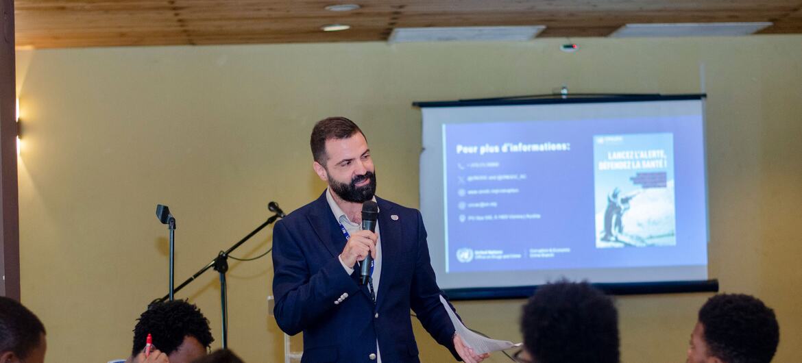 A man in a suit speaks at a presentation to an audience in a classroom setting.