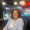 Tania Romualdo sorri para uma foto enquanto está sentada em um estúdio de gravação de podcast.