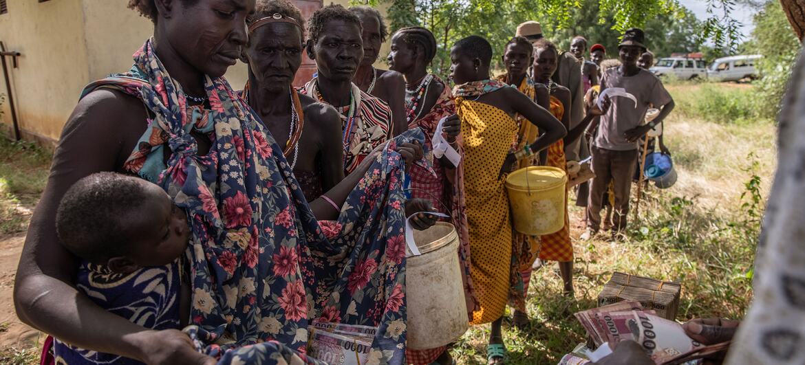 Mulheres sul-sudanesas e uma criança aguardam na fila para receber assistência financeira durante uma distribuição de ajuda humanitária em Kapoeta Norte.