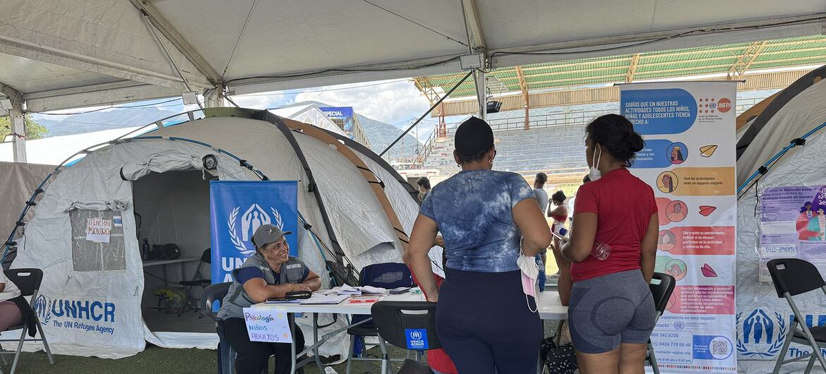 Un miembro del personal del ACNUR ayuda a los refugiados en un mostrador de registro bajo una carpa en un campamento de refugiados en Venezuela.