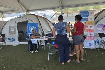 Un miembro del personal del ACNUR ayuda a los refugiados en un mostrador de registro bajo una carpa en un campamento de refugiados en Venezuela.