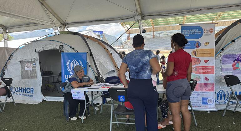 Un miembro del personal del ACNUR ayuda a los refugiados en un mostrador de registro bajo una carpa en un campamento de refugiados en Venezuela.