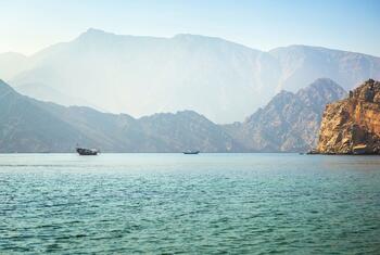 A traditional dhow boat on the water with mountains in the background near Musandam, Oman.