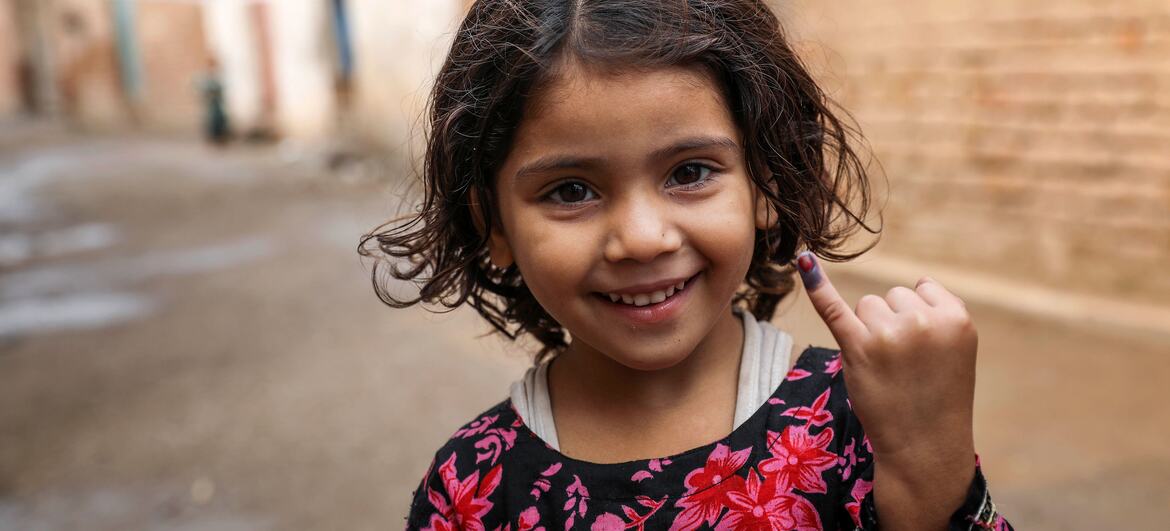 پاکستان میں UNICEF مہم میں خسرہ کی ویکسینیشن حاصل کرنے کے بعد ایک نوجوان لڑکی فخر سے اپنی انگلی پر جامنی رنگ کی سیاہی کا نشان دکھا رہی ہے۔