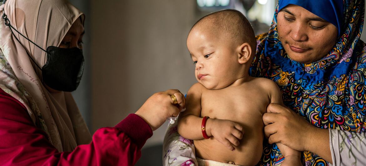 A health worker administers a vaccine to a one-year-old child held by his mother during a house-to-house vaccination campaign in the Philippines.