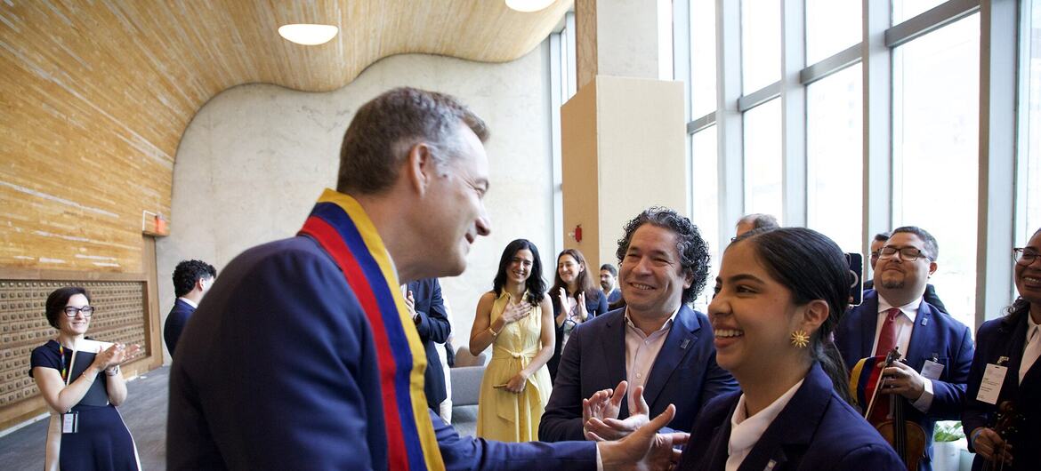 El responsable del PNUD estrecha la mano de una mujer vestida de traje en un acto formal, mientras el público aplaude y hay músicos de fondo.