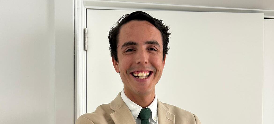 Retrato de um homem sorridente vestindo um terno bege e gravata verde.