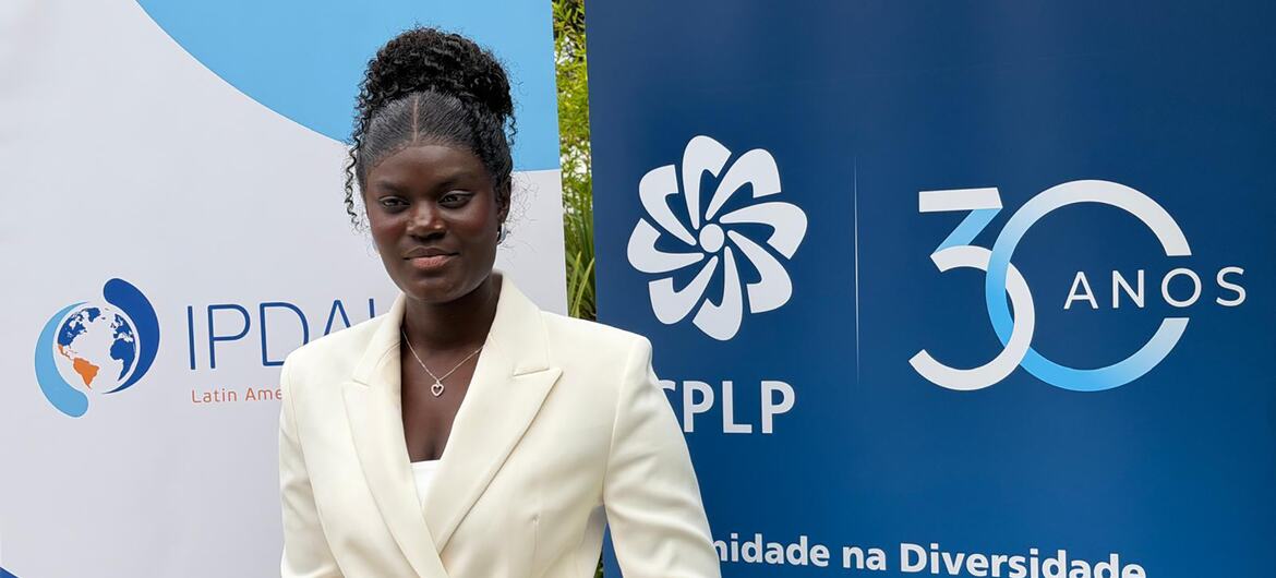 Luísa Aminata posa em frente às faixas da CPLP que celebram 30 anos de comunidade para os povos.