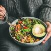 Женщина в свитере и джинсах держит миску с салатом из авокадо и нута.