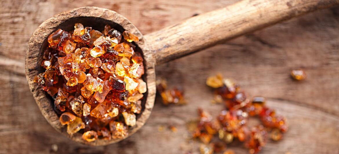 Gum arabic, also known as acacia gum, in a wooden spoon on a wooden surface.