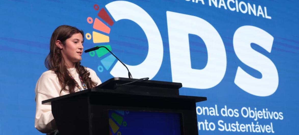 Uma jovem discursa em um pódio durante a 1ª Conferência Nacional sobre a Síndrome da Destruição da Superfície Ocular (SDO) no Brasil.