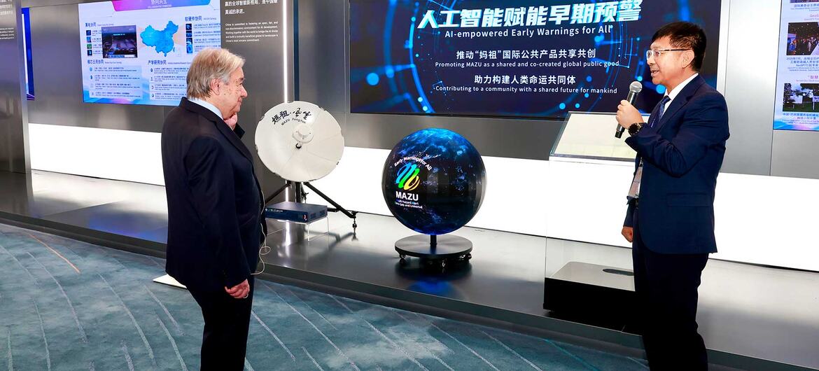 En una exposición de tecnología, un hombre de traje habla por un micrófono mientras otro escucha; una gran pantalla muestra un sistema de alerta temprana meteorológica basado en inteligencia artificial.