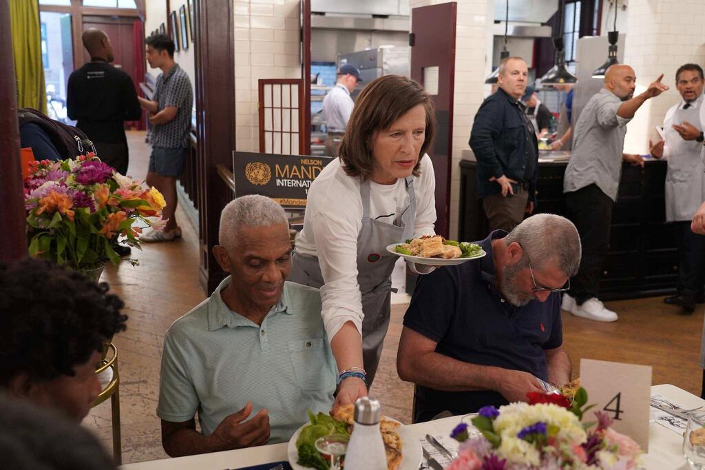 A United Nations volunteer serves food to guests at a community meal event at Refettorio Harlem.