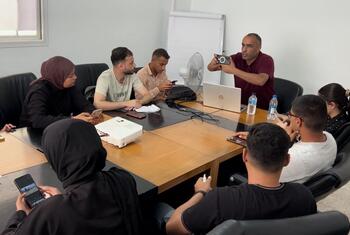 يقوم مدرب بتوضيح تقنيات التعامل السليم مع الكاميرا خلال جلسة تدريبية في مجال الصحافة المتنقلة مع المشاركين في قاعة المؤتمرات.