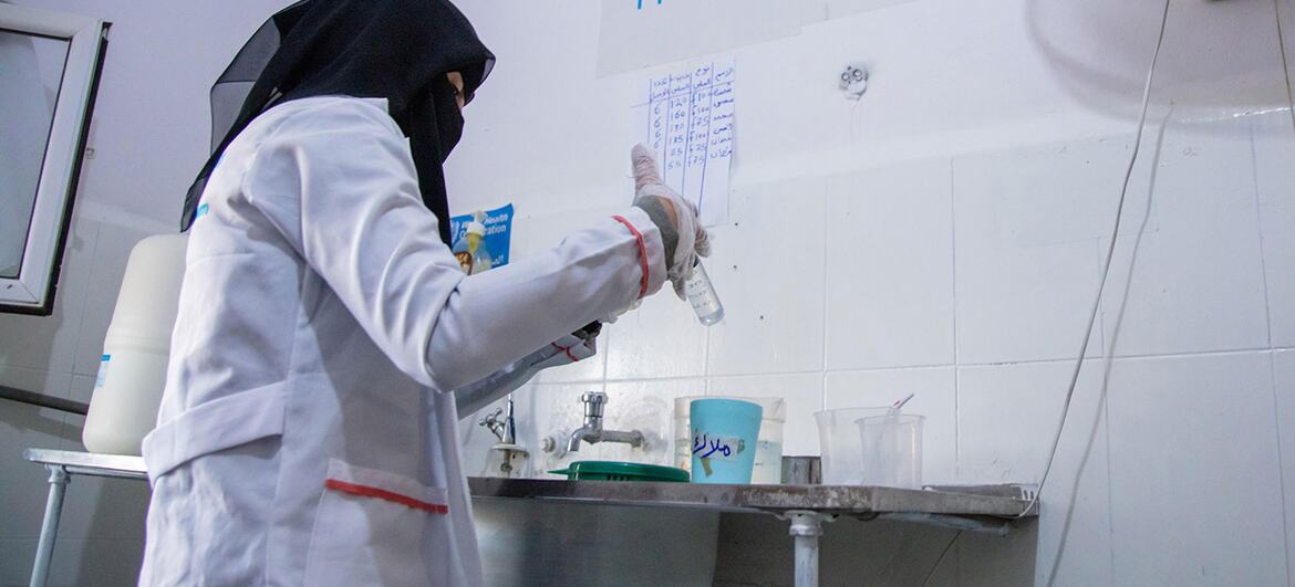 A female medical professional in a white coat and gloves prepares medication at a clinic in Yemen.