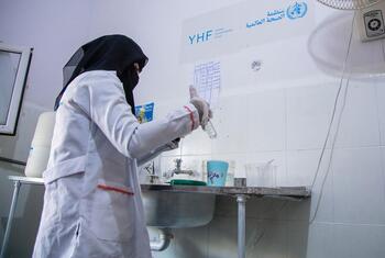 A female medical professional in a white coat and gloves prepares medication at a clinic in Yemen.