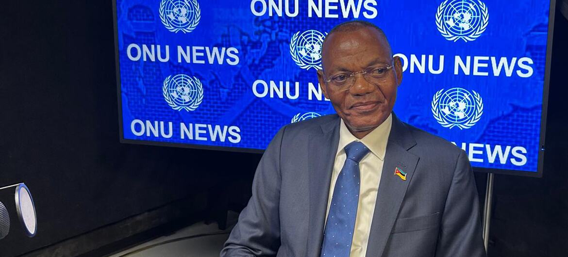 Um homem de terno e gravata está sentado em um estúdio em frente a uma tela azul com a inscrição 'ONU NEWS'.