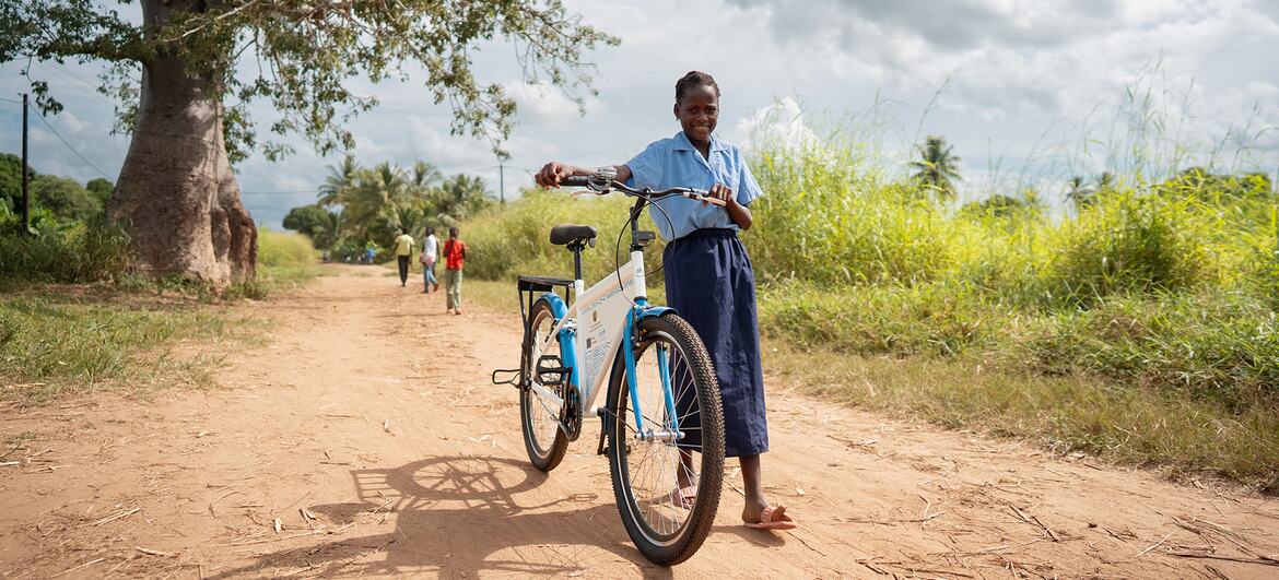 Uma menina de uniforme escolar está em uma estrada de terra com uma bicicleta da Unicef em Moçambique.