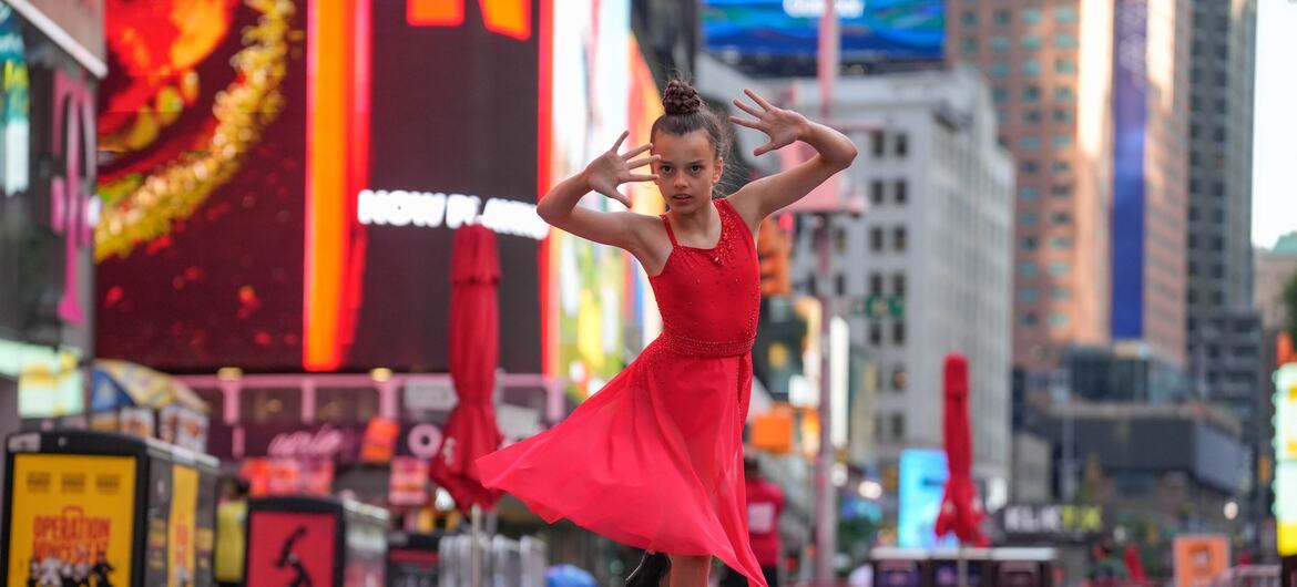 A young Ukrainian girl in a red dress performs a dance on a city street, using a prosthetic leg.