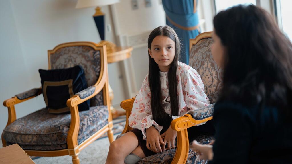 Une jeune fille ukrainienne vêtue d'un chemisier à fleurs est assise dans un fauteuil orné et discute avec une femme assise en face d'elle.